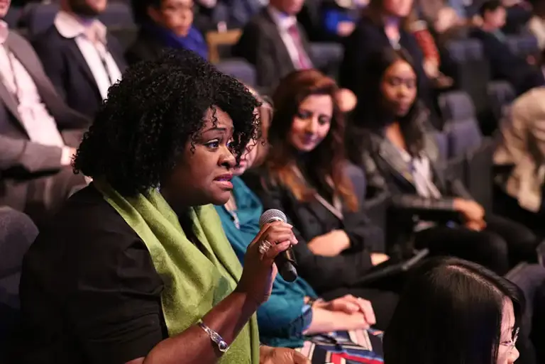 Woman in the audience of a large conference in a lecture hall stands with the microphone to ask her question 
