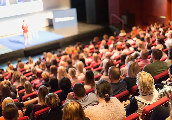 View from the back of packed auditorium with looking towards the speaker on the stage below 