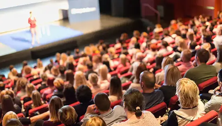 View from the back of packed auditorium with looking towards the speaker on the stage below 